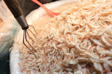 Canvas Print - Close-up of stacled salt-pickled shrimps made in June for sale with a mixing tool at a traditional fish market, South Korea
