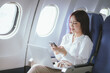 © Witoon - A woman sits comfortably by the airplane window, smiling as she travels. With her laptop open, she combines work and relaxation, embodying the modern lifestyle of a successful business traveler.
