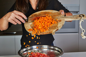 Sticker - Close-up of hands using a knife to throw fresh carrots from a wooden cutting board into a pan in the kitchen