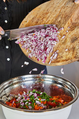 Poster - Close-up of hands using a knife to throw fresh onions from a wooden cutting board into a pan in the kitchen