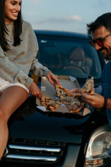 Canvas Print - Urban styled couple easting a slice of pizza on a car and enjoying the sunset