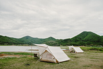 White camping picnic tent campground in outdoor park lake with mountains and blue sky with white clouds in the background. Adventure travel and vacation concept
