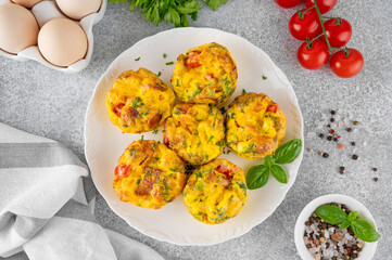 Wall Mural - Egg muffins or egg bites with bacon, cheese, vegetables and herbs on a white plate on a concrete background. Healthy breakfast.