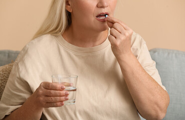 Sticker - Beautiful mature woman with glass of water taking pill at home