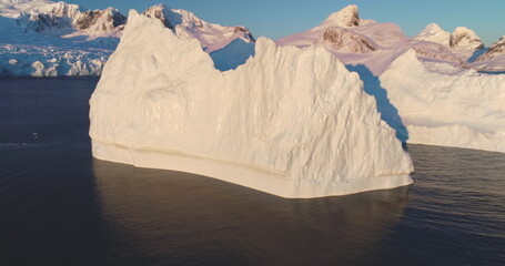 Wall Mural - Frozen ice wall drifting Antarctica ocean bay in sunrise morning light. A massive iceberg floating icy polar water. Snow covered mountains in background. Global warming, climate change. Panoramic shot