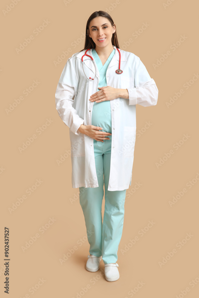 Beautiful young pregnant doctor on brown background