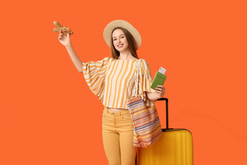 Poster - Smiling young woman with wooden airplane and passport on orange background. Travel concept