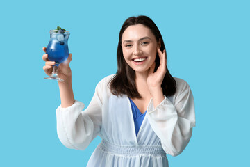 Poster - Beautiful young woman holding glass of tasty cocktail with blueberry on blue background