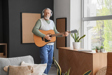 Wall Mural - Mature man in headphones playing guitar at home