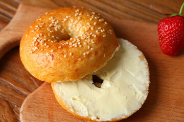 Wall Mural - Board of tasty bagel with butter and strawberry on wooden background