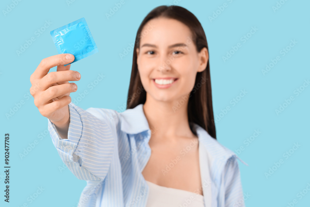 Young woman with condom on blue background, closeup