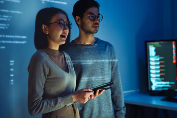 Wall Mural - Asian Two software developers engaged in collaborative coding session, with code projected onto the wall and multiple computer screens displaying