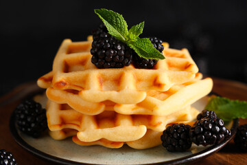 Wall Mural - Delicious Belgian waffles with blackberries on board on black background. Closeup