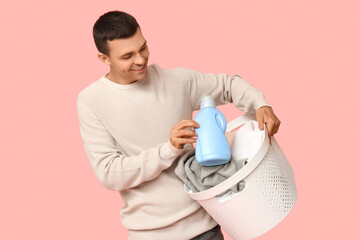 Sticker - Young man with laundry basket and bottle of detergent on pink background