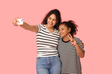 Canvas Print - Beautiful young happy African-American mother and her daughter with mobile phone taking selfie on pink background