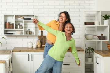 Sticker - Beautiful young happy African-American mother with her daughter in kitchen at home