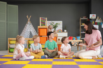 Wall Mural - Nursery teacher reading story to little children in kindergarten