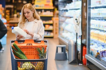 young woman in casual clothes shopping at supermaket grocery store buy choose dairy produce take mil