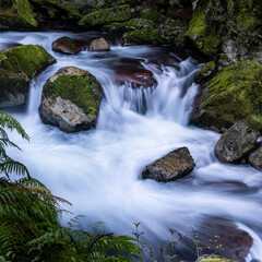 waterfall in the mountains with running water and moss on the rocks in the water