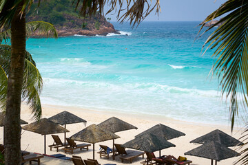 Turquoise sea waves crashing on idyllic tropical beach with palm trees and umbrellas