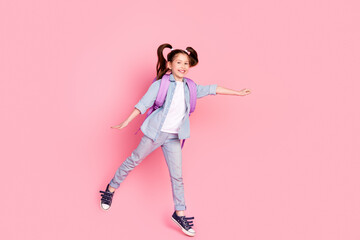 Wall Mural - Full size photo of positive lovely small girl dressed denim shirt rucksack on shoulders jumping to empty space on pink color background