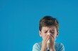 © Rzk Studio - boy sneezing with tissue on blue background. Allergic kid, flu season. Kid with cold rhinitis.