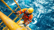 © Anastasiia Havelia - A worker in an orange safety suit climbing on the yellow metal and rope of an ocean rig, working at sea with a blue water background.