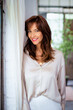 © sepy - Close-up portrait of an attractive brunette haired woman standing at the window and smiling
