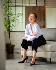 Poster - Ful length of a beautiful mid aged woman relaxing in an armchair by the window