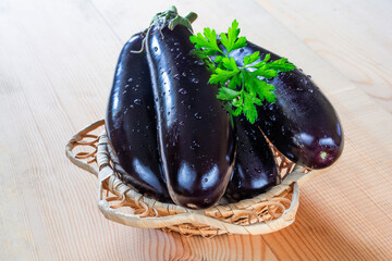 Wall Mural - Fresh ripe eggplants in a wicker bowl on a wooden background