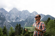 © Kateryna Muzhevska - a satisfied man in a checkered shirt holds a map of the area in his hands and looks into the distance at the high mountains on a sunny day