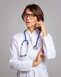 © sepy - Attractive mid aged female doctor with smarpthone standing against isolated background