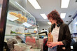 © Oscar - A woman is shopping in a store and is holding a bag. The store has a display case with various food items