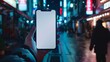 © MD Media - Mockup of a blank smartphone, mobile phone screen held in hand, hand holding a blank smartphone in front of a blurred background of a busy city street at night