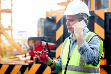 Senior worker engineer foreman with safety vest and helmet talking on mobile phone while working at construction site. Mature elderly architect works at ground level of building workplace.