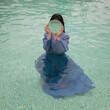 © Milou Dirks - art portrait of woman in long blue dress standing in middle of swimming pool holding round mirror