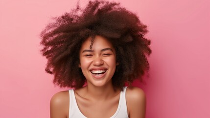 Wall Mural - A woman with curly hair is smiling and laughing. She is wearing a white tank top and is standing in front of a pink background