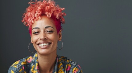 Vibrant portrait of a joyful woman with striking pink curly hair, wearing a colorful patterned shirt, radiating confidence and warmth against a dark background.