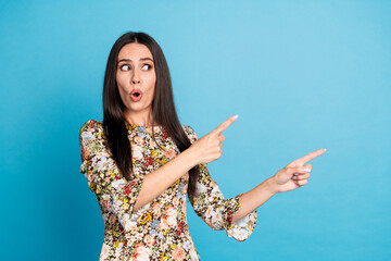 Poster - Photo of impressed positive woman wear print dress pointing looking empty space isolated blue color background