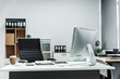 © Phushutter - A modern, white-colored business office with a wooden desk, calculator, desktop computer, and a black leather chair. The executive office features private office furniture for the chief of staff.