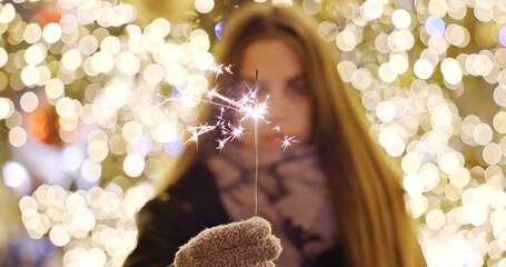 Woman holding sparkler with festive lights background