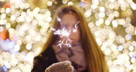 Woman holding sparkler with festive lights background