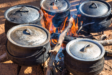 african street vendor cooking in the cauldron three legged pot outdoors cooking, running a small business in the outdoors kitchen