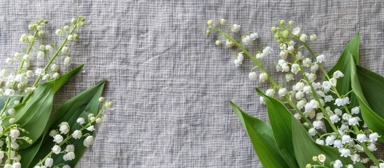 Poster - Top view of a rustic greeting card concept with a bouquet of white lilies of the valley and green leaves on a gray linen background offering ample copy space for cover design