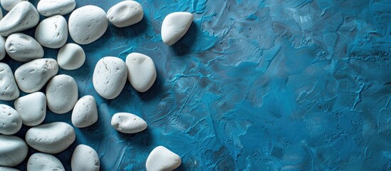 Poster - A messy arrangement of white textured pebbles on a blue table with copy space image