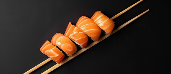 Aufkleber - Sushi pieces held by chopsticks on a black backdrop with a copy space image for a creative Japanese cuisine concept Top down view