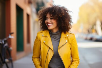 Wall Mural - Portrait of a joyful afro-american woman in her 20s sporting a classic leather jacket isolated in pastel yellow background