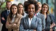 © Blackmint Studio - A confident woman stands at the front of a diverse group of six business professionals smiling with arms crossed outside a modern office building