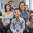 © Hanna - Young Boy Smiling Sitting in Front of Group of Adults in Office Setting.