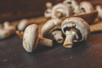 Champignon mushrooms in a wooden plate on a dark background